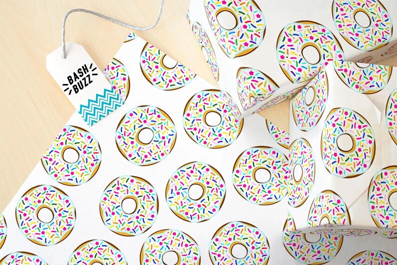 K&ouml;nnte beinhalten: Wei&szlig;es Geschenkpapier mit einem sich wiederholenden Muster aus bunten Donuts mit Streuseln. Die Donuts sind hellblau mit wei&szlig;em Zuckerguss und bunten Streuseln. Das Papier hat den Text "Bash Buzz" auf einem blau-wei&szlig;en Etikett.