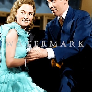 May include: A woman in a light blue ruffled dress and a man in a dark blue suit are smiling and holding hands. The man is wearing a white shirt and a yellow patterned tie.