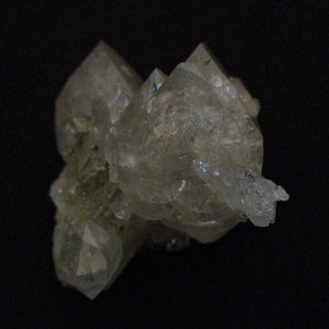 Può includere: Un gruppo di cristalli di quarzo traslucidi e di colore chiaro su sfondo nero. I cristalli presentano terminazioni appuntite e una consistenza leggermente ruvida, che mostra formazioni geologiche naturali.