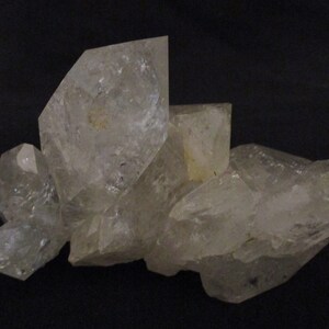 Puede incluir: Un grupo de cristales de cuarzo transparente con una estructura cristalina. El cuarzo tiene una apariencia translúcida y está sobre un fondo oscuro. Los cristales varían en tamaño y forma.