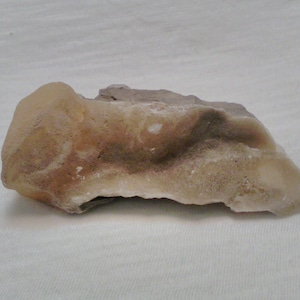 May include: A light brown, irregularly shaped rock with a rough, textured surface. The rock has a white, crystalline appearance in some areas.