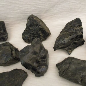 May include: A collection of black, rough, and irregularly shaped stones. The stones have a dark, almost metallic sheen.