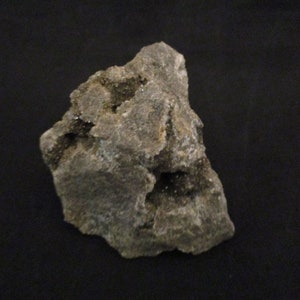 May include: A grey rock formation with a textured surface and an irregular shape. The rock appears to be a mineral specimen. The background is a solid black.