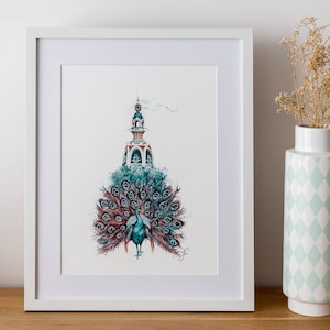 Peut inclure: Une impression encadrée blanche d'une illustration aquarelle d'un paon avec une queue bleue et verte. Le paon se tient au sommet d'un petit bâtiment blanc avec un toit bleu. L'impression est sur une table en bois avec un vase de fleurs séchées.