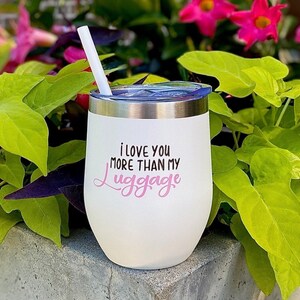 Puede incluir: Un vaso de vino de acero inoxidable blanco con una inscripci&oacute;n rosa que dice "Te amo m&aacute;s que a mi equipaje".