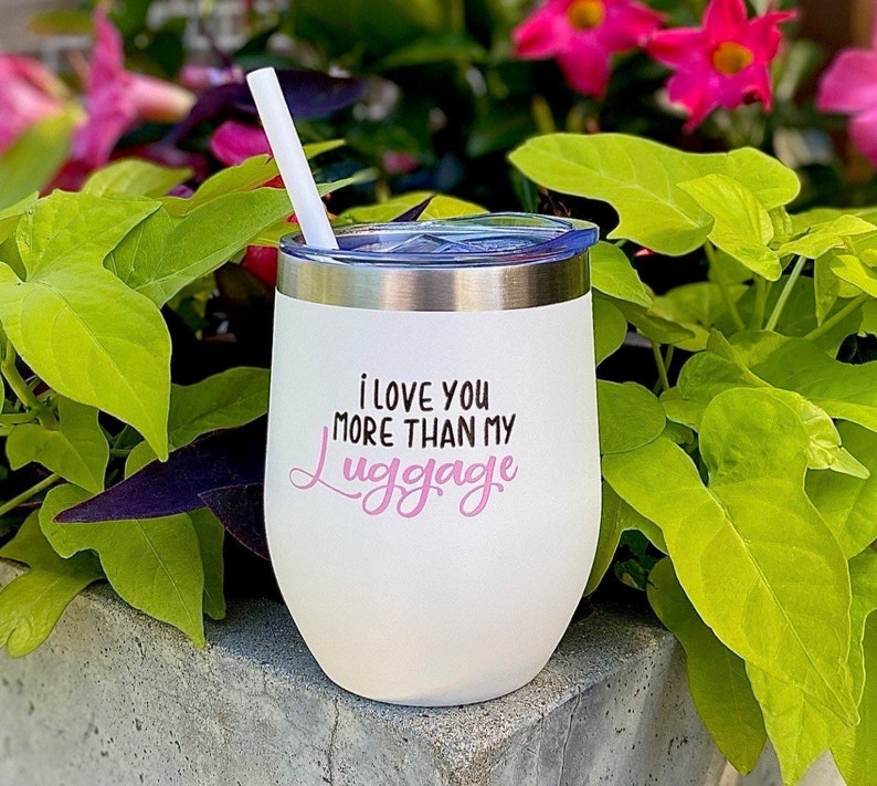 Puede incluir: Un vaso de vino de acero inoxidable blanco con una inscripci&oacute;n rosa que dice "Te amo m&aacute;s que a mi equipaje".