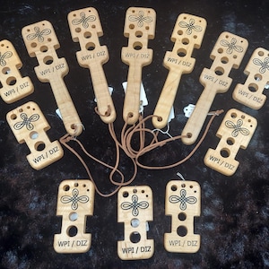 May include: Ten wooden tools with a knotted design and holes. Each tool has a leather cord attached and the text "WPI/DIZ" is engraved on each tool.