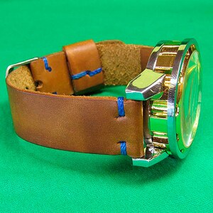 May include: A brown leather watch band with blue stitching and a gold and silver watch face.