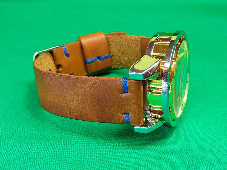 May include: A brown leather watch band with blue stitching and a gold and silver watch face.