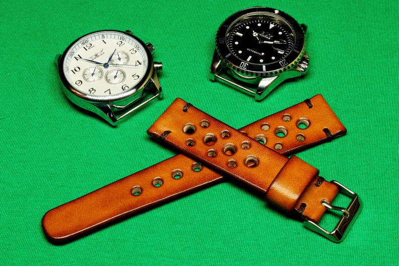 May include: Two wristwatches with brown leather watch bands with holes. The watch bands are crossed over each other. The watch bands have silver buckles. One watch has a white face with black hands and black numbers. The other watch has a black face with silver hands and silver numbers.