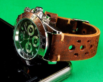 Puede incluir: Un reloj de pulsera cronógrafo plateado con una esfera negra y una correa de cuero marrón con agujeros. El reloj está sobre una superficie negra.