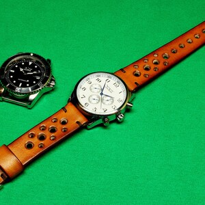 May include: A brown leather watch strap with holes and a silver chronograph watch with a white face. The watch strap has a buckle closure.