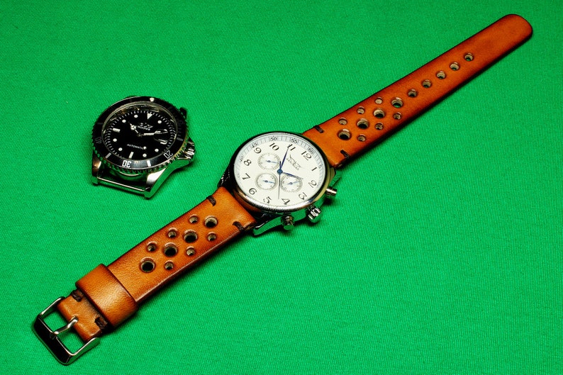 May include: A brown leather watch strap with holes and a silver chronograph watch with a white face. The watch strap has a buckle closure.