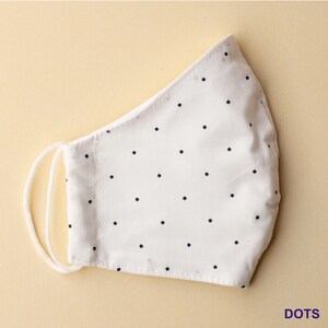 May include: White face mask with small black polka dots. The mask has a white elastic band.