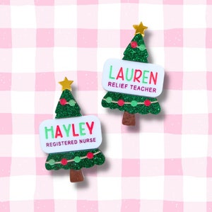 May include: Two Christmas tree-shaped ornaments with glitter. One ornament has the name "HAYLEY REGISTERED NURSE" on it. The other ornament has the name "LAUREN RELIEF TEACHER" on it.