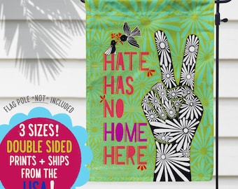 May include: A green garden flag with a peace sign made of white daisies and the text "Hate Has No Home Here" in colorful letters.