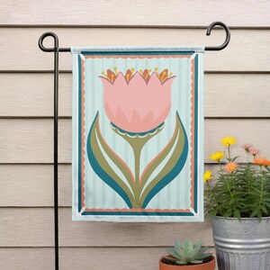 Peut inclure: Un drapeau de jardin d&eacute;coratif avec un motif de tulipe rose stylis&eacute;e. La fleur a un centre d&eacute;taill&eacute; et se d&eacute;tache sur un fond &agrave; rayures bleu clair. Le drapeau est encadr&eacute; d'une bordure festonn&eacute;e et d'accents turquoise.