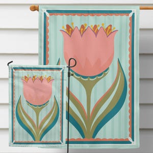 Peut inclure: Deux drapeaux de jardin avec un motif floral. Les drapeaux pr&eacute;sentent une grande tulipe rose avec des feuilles vertes et bleues sur un fond &agrave; rayures bleu clair. Les drapeaux sont encadr&eacute;s d'une bordure festonn&eacute;e.