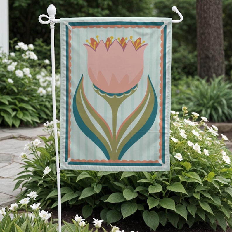 Peut inclure: Un drapeau de jardin avec un motif de tulipe rose et des accents turquoise et verts. Le drapeau a un fond &agrave; rayures bleu clair et une bordure festonn&eacute;e. Il est affich&eacute; sur un support en m&eacute;tal blanc, entour&eacute; de verdure et de fleurs blanches.