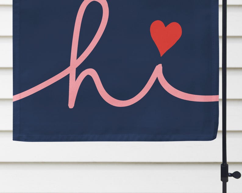 Pode incluir: Uma bandeira de jardim azul marinho com a palavra "hi" em fonte cursiva rosa claro. Um cora&ccedil;&atilde;o vermelho est&aacute; acima do "i". A bandeira est&aacute; pendurada em um poste de metal preto contra um fundo branco.