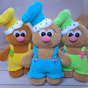 May include: Three crocheted plush toys shaped like gingerbread people. The toys are wearing different colored overalls and hats. The toys are brown, yellow, and green.