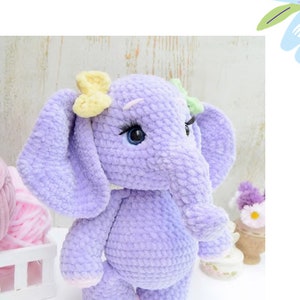May include: A crocheted purple elephant plush toy with yellow and green bows. The elephant has blue eyes and pink feet.