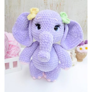 May include: A crocheted purple elephant plush toy with yellow and green flower accents. The elephant has a long trunk and large ears.