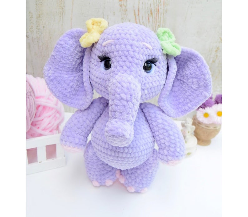 May include: A crocheted purple elephant plush toy with yellow and green flower accents. The elephant has a long trunk and large ears.