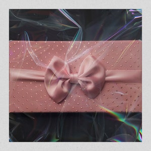 May include: A pink gift box with a satin bow. The box is covered in small pink dots and has a clear plastic wrap over it.