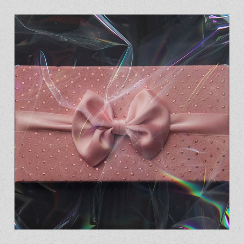 May include: A pink gift box with a satin bow. The box is covered in small pink dots and has a clear plastic wrap over it.
