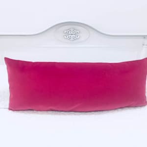 May include: A bright pink velvet lumbar pillow on a white bed.