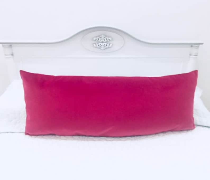 May include: A bright pink velvet lumbar pillow on a white bed.