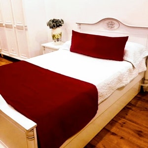 May include: A white bed frame with a red throw blanket and a red pillow. The bed is in a room with white walls and a white closet.