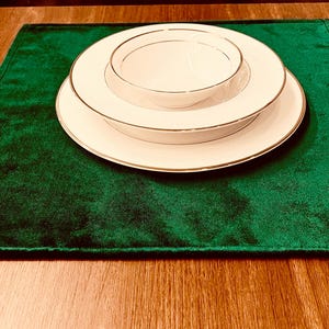 Könnte beinhalten: Ein Satz aus drei weißen Keramiktellern mit goldenen Rändern, auf einem grünen Samt-Platzset.