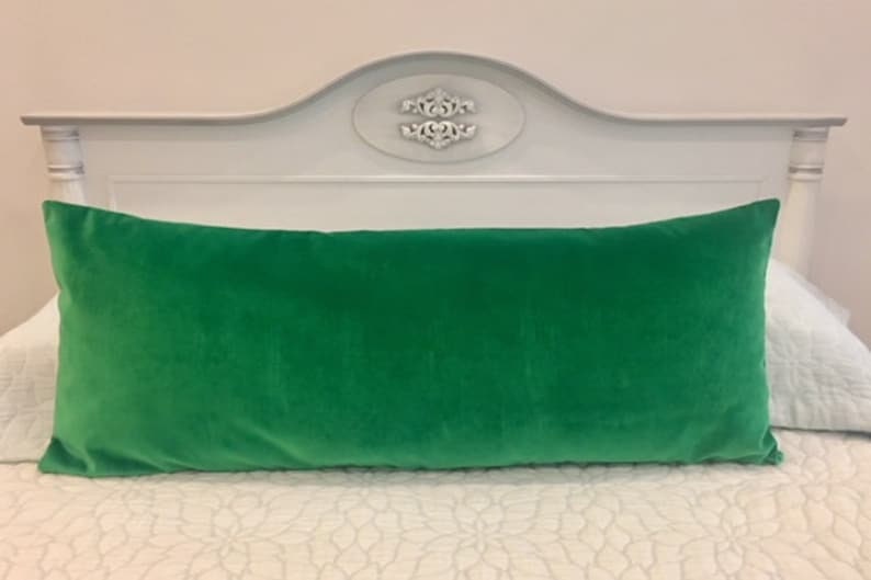 May include: A bright green velvet lumbar pillow on a white bed with a white headboard.