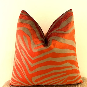 May include: A decorative throw pillow with a vibrant orange and gray zebra stripe pattern. The pillow is square-shaped and rests on a tufted surface, adding a touch of modern flair to home decor.