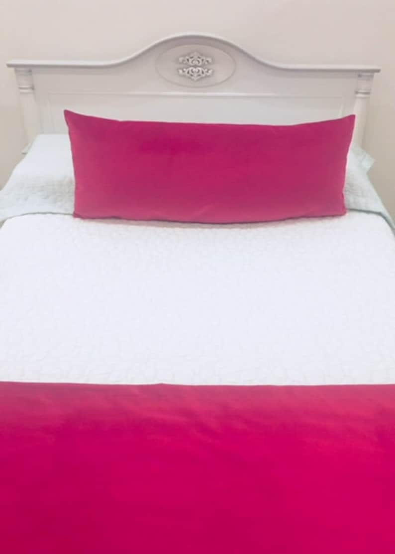 May include: A white bed with a pink pillow and a pink bed skirt. The headboard is white with a decorative design.