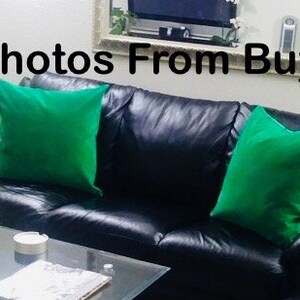 May include: A black leather sofa with two green throw pillows. The sofa is in a living room setting with a coffee table in front of it.