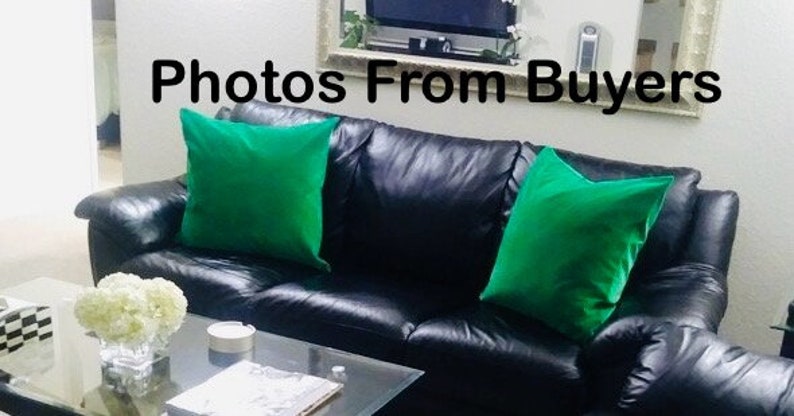 May include: A black leather sofa with two green throw pillows. The sofa is in a living room setting with a coffee table in front of it.