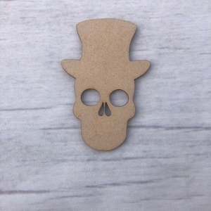May include: A wooden cutout of a skull wearing a top hat. The skull has two eye sockets and a nose.
