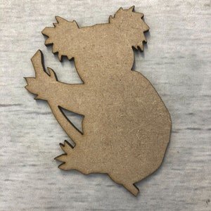 May include: A wooden cutout of a koala bear sitting on a branch. The cutout is unpainted and ready to be decorated.