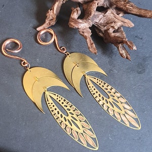 May include: A pair of gold-toned metal earrings with a spiral design and a dangling crescent moon and leaf-shaped charm. The earrings are made of brass and have a copper-toned spiral.