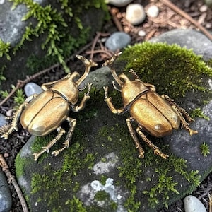 以下が含まれることがあります： 詳細な足と触角を持つ2つの金色のカブトムシの彫刻が、苔で覆われた岩の上に配置されています。 カブトムシは互いに向き合い、さらに苔、岩、小石を背景に、自然なシーンを作り出しています。