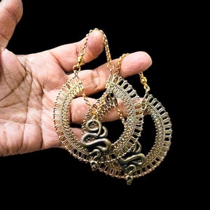 May include: A pair of gold hoop earrings with a snake design dangling from the bottom. The earrings are made of a delicate, intricate metalwork.