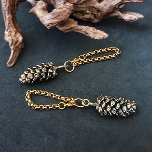 May include: Two gold chains with a pine cone charm on each end. The pine cones are silver and have a detailed design.