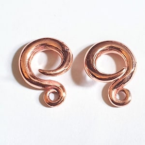May include: A pair of rose gold spiral ear gauges. The gauges are made of metal and have a smooth, polished finish.