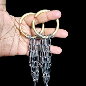 Puede incluir: Un par de pendientes de aro dorados con cadenas plateadas colgantes y puntas puntiagudas.