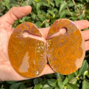 Puede incluir: Un par de tapones grandes, redondos, de ágata naranja y marrón con un agujero en el centro. Los tapones son lisos y pulidos.