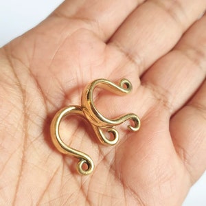May include: Gold-toned metal nose ring with a unique, intricate design. The ring is shaped like a double loop with a smaller loop at the end of each larger loop.