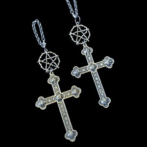 May include: Two silver and gold cross pendants with pentagram charms hanging from silver chains. The crosses have intricate designs and are detailed with black accents.